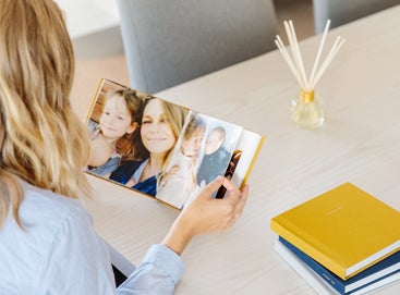 Woman at table flipping through Everyday Photo Book filled with kids' photos