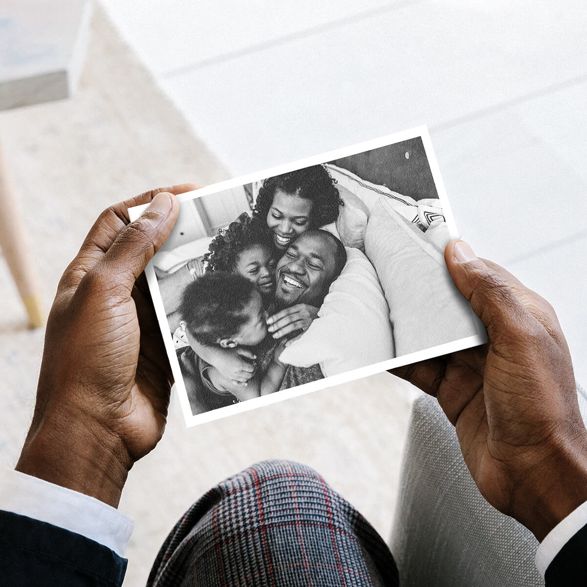 Hands holding DIY postcard with photo of family laughing and lounging on bed