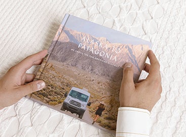 Hands holding Artifact Uprising Photo-Wrapped Hardcover Book titled Alaska to Patagonia featuring photo of camper van in front of mountainous landscape