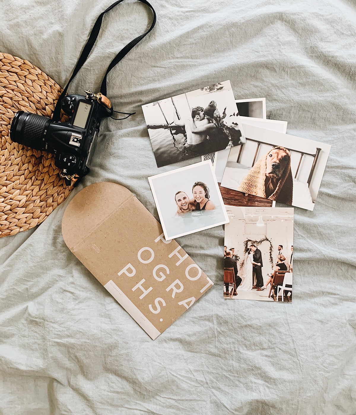 Photo prints on bed next to camera and hat